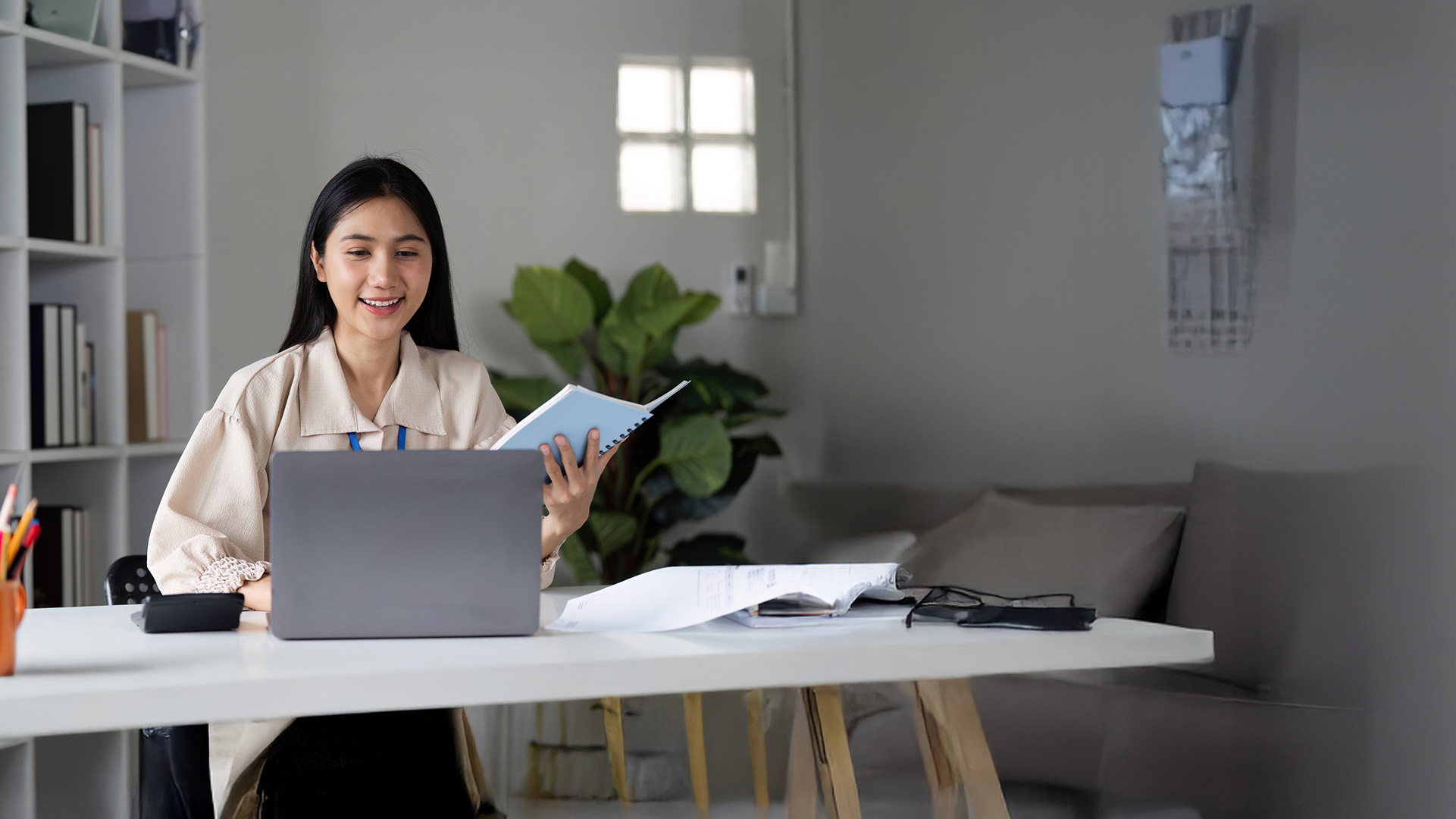 Lady sitting at desk with laptop and a notebook in hand