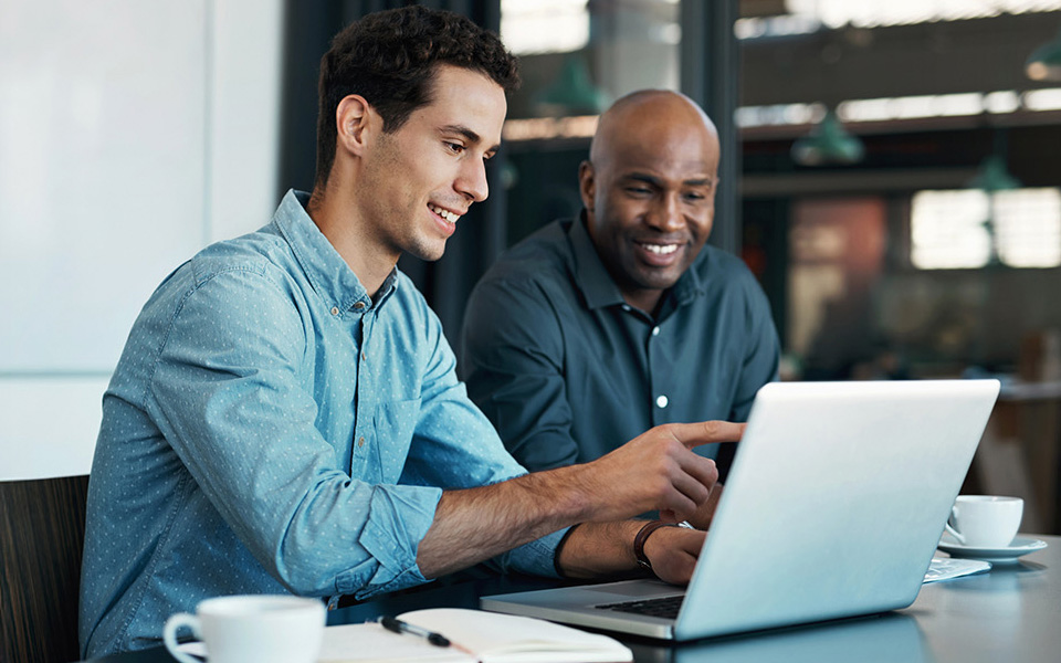 Two co-workers discussing something sat at a desk on a laptop
