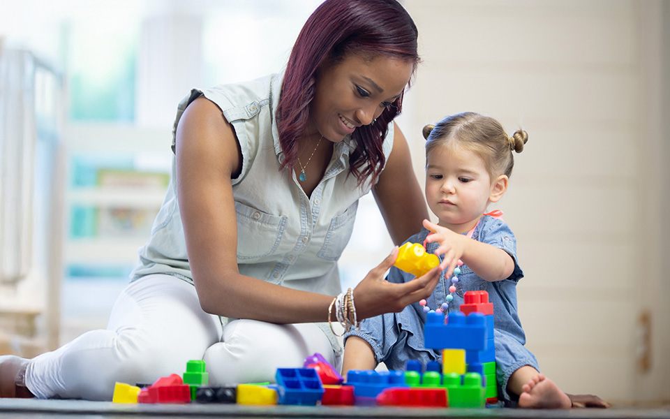 Female nursery worker playing with a child with building blocks