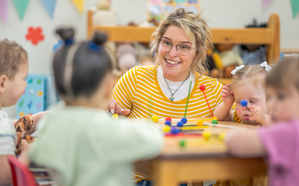 Female nursery worker playing at table with children