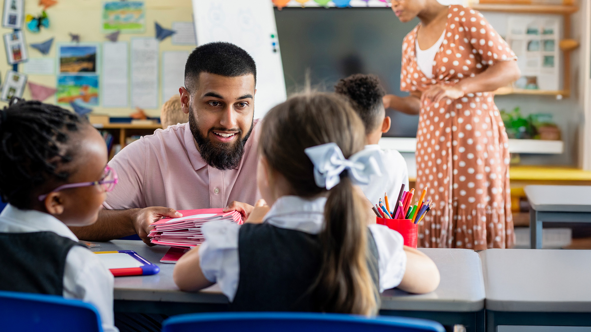 Male teaching assistant with two pupils in a primary school classroom