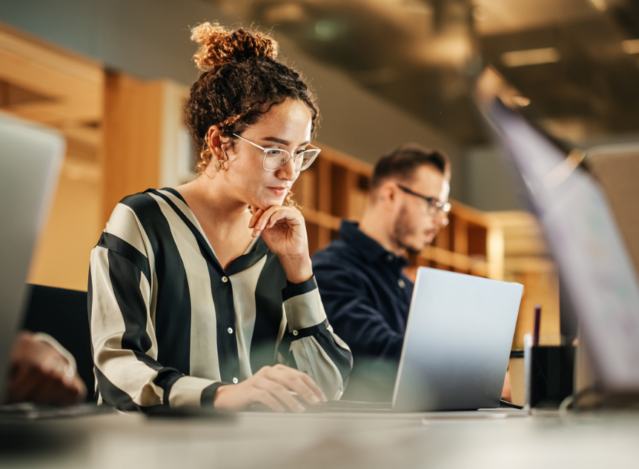 Woman in an office setting looking at a laptop with a strong concentration face.