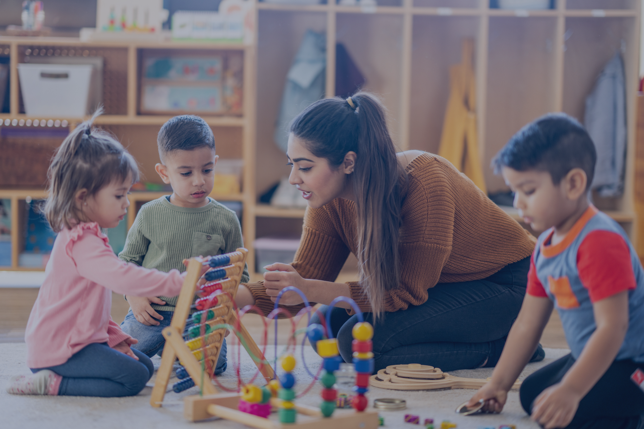 A nursery teaching with a group of 3 toddlers playing with colourful wooden toys