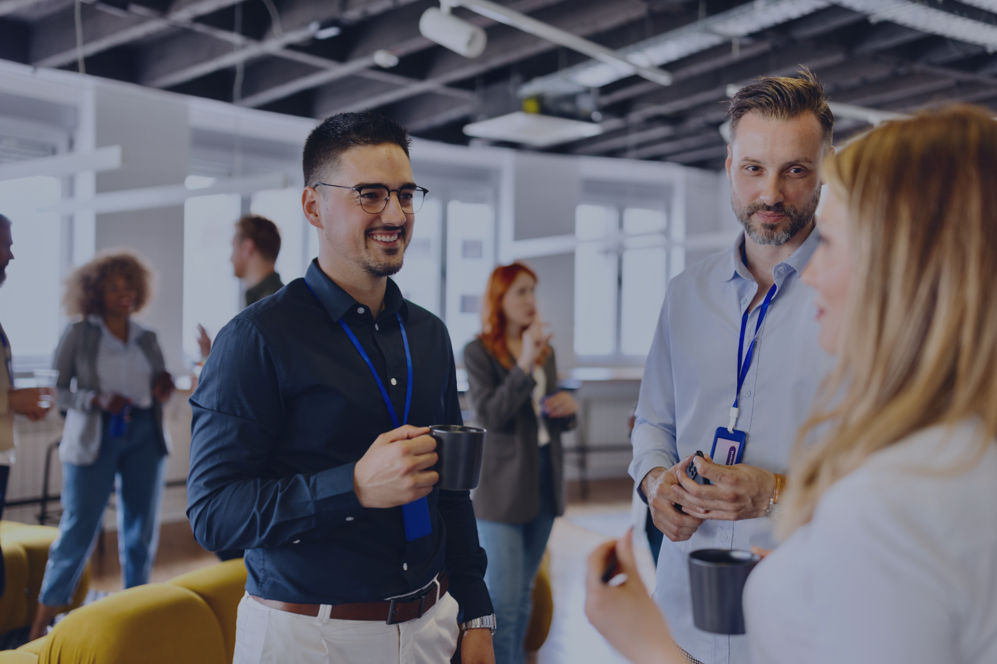 Three people having a conversation in an office. Some people in the foreground of the office having conversations