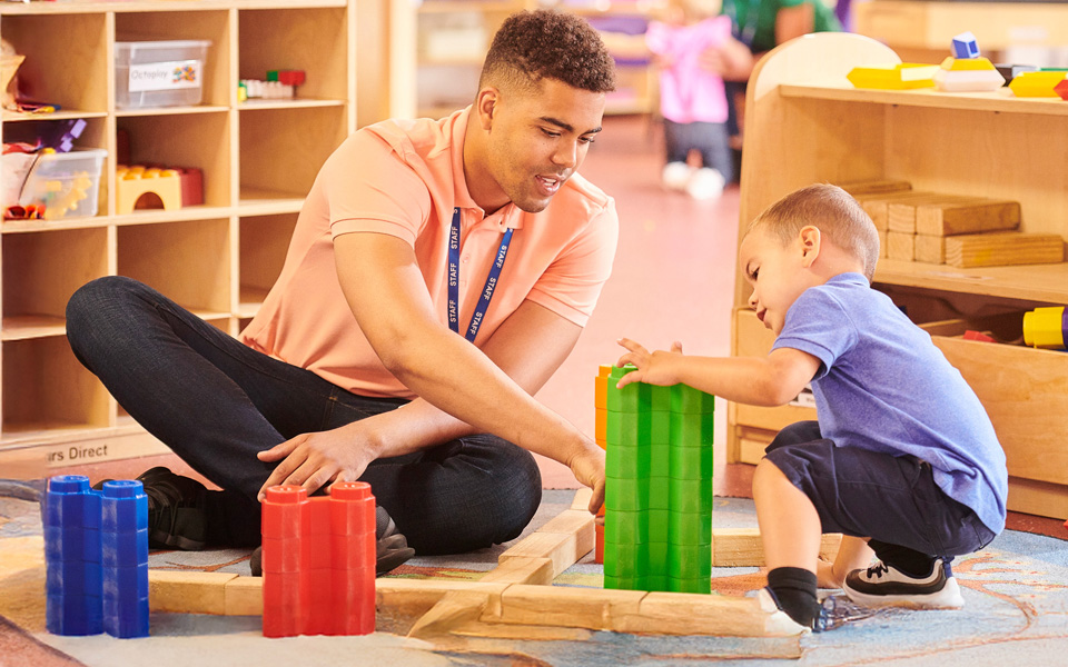 Male nursery worker playing with building bricks with a child