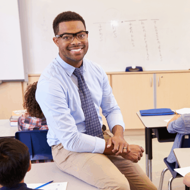A young man wearing a smart shirt and tie sitting on a desk and smiling